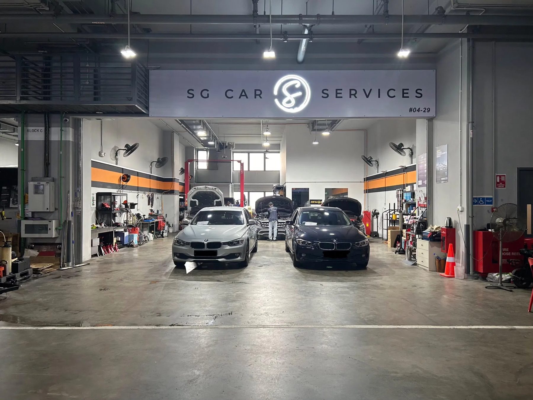 The SG Car Services workshop at Carros Centre, with cars on ramps under the workshop signage